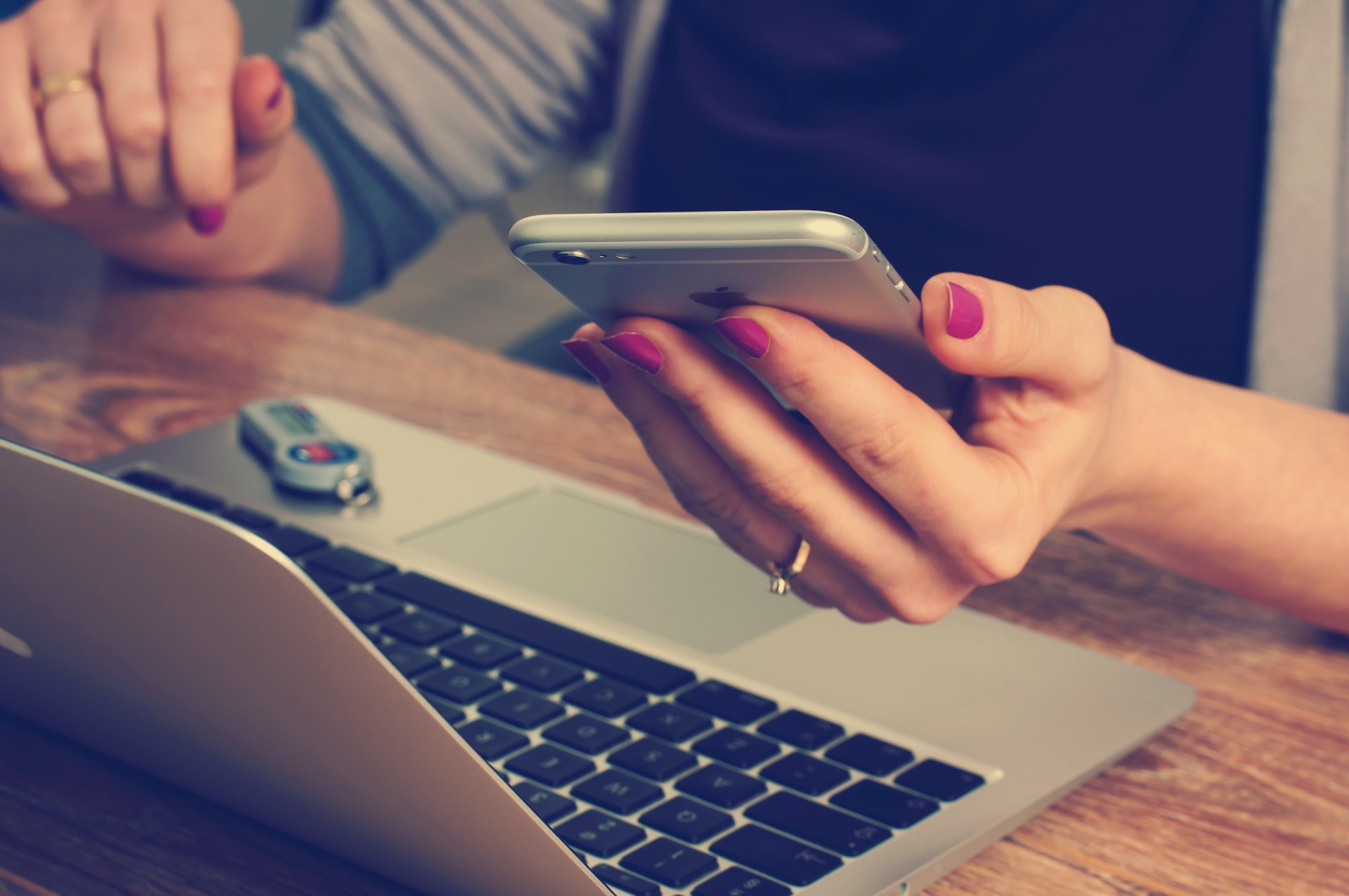 Close up of a person holding a phone while also using their laptop